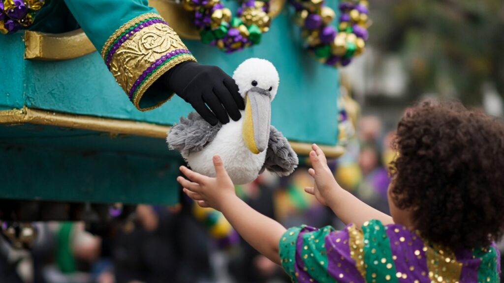 A float rider's gloved hand passing a plush pelican to a child